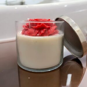 Decorative jar candle with a rose-shaped wax topper and soy wax base in a clear glass jar with a metallic lid.